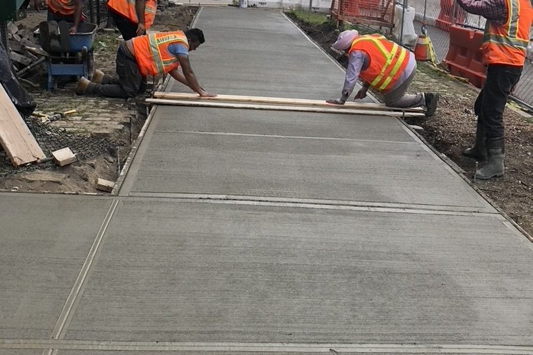 NYC sidewalk crew finishing a freshly poured concrete sidewalk to DOT standards